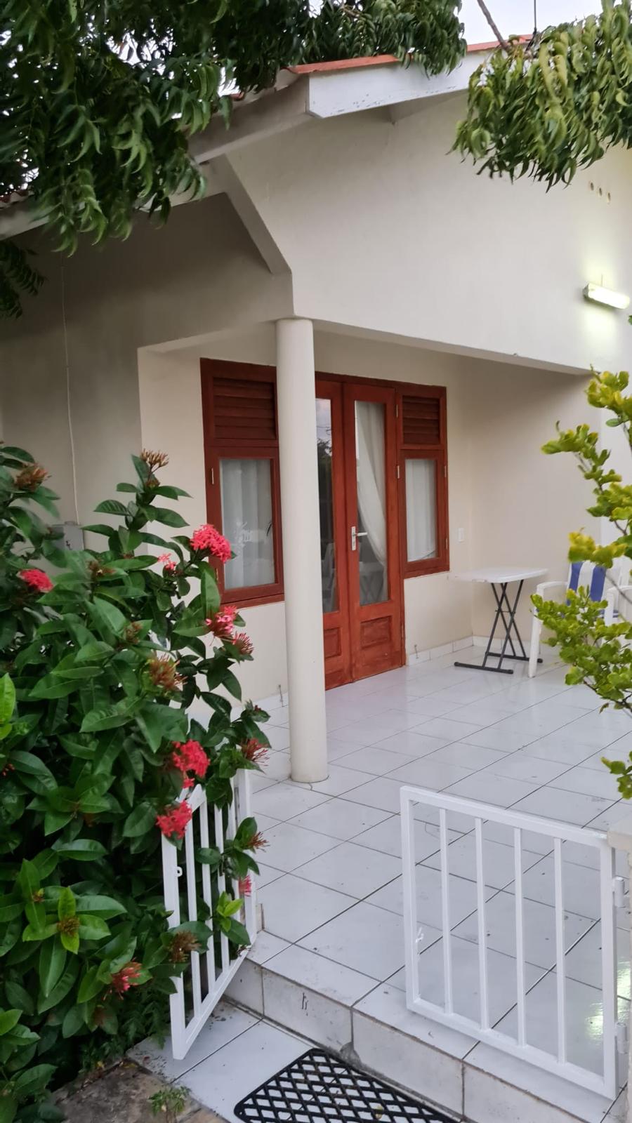 Modern white "Casa Gioia" villa with dark windows, covered porch, palm trees, and pink bougainvillea under a clear blue sky. Paved entrance.